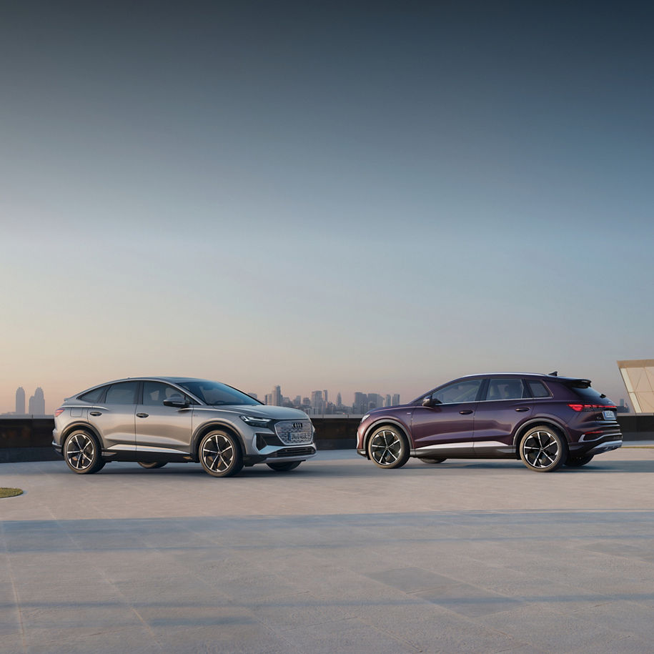 Two parked Audi electric vehicles parked and facing each other with a cityscape in the distance